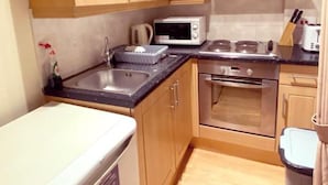 A compact kitchen with wooden cabinets, a stainless steel range hood, a microwave, an oven, and a small refrigerator. - London Chelsea, Big 2 People Studio Apartment (London)