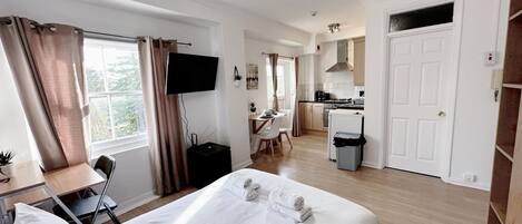 Quarto de hotel com cama, escrivaninha com cadeira, televisão, cozinha compacta e banheiro.