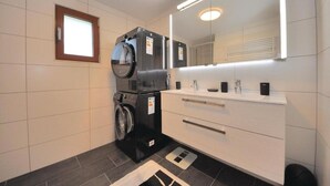 A modern bathroom with a washing machine, a sink, and a mirror.