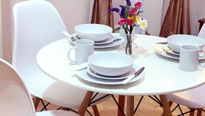 Ein runder Esstisch mit weißen Tellern, Schüsseln und einer Tasse, umgeben von weißen Stühlen.