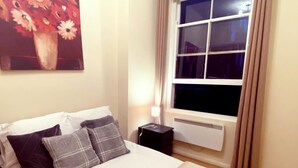 Ein Schlafzimmer mit einem Bett, einem Nachttisch, einem Heizkörper und einem Fenster mit Vorhängen.