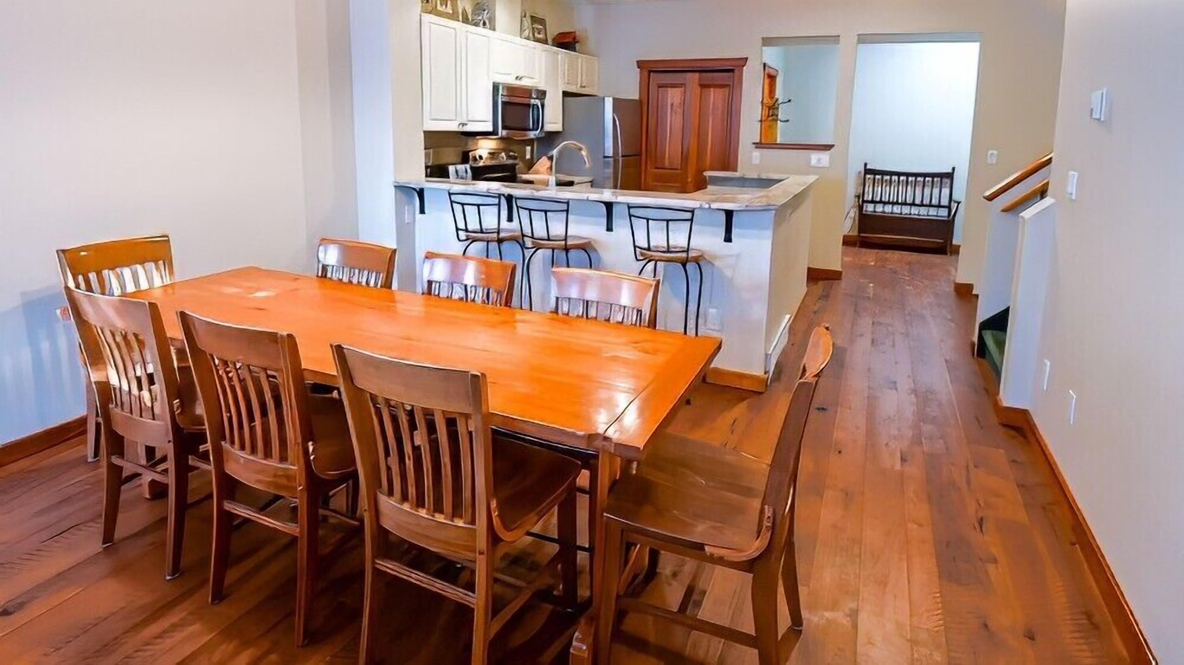 Un coin repas avec une table et des chaises en bois, une cuisine avec des meubles blancs et une porte en bois, et un plancher en bois.