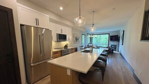 Een moderne keuken met een groot eiland, roestvrijstalen apparatuur en hanglampen.