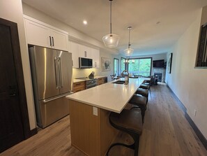 Een moderne keuken met een groot eiland, roestvrijstalen apparatuur en hanglampen.