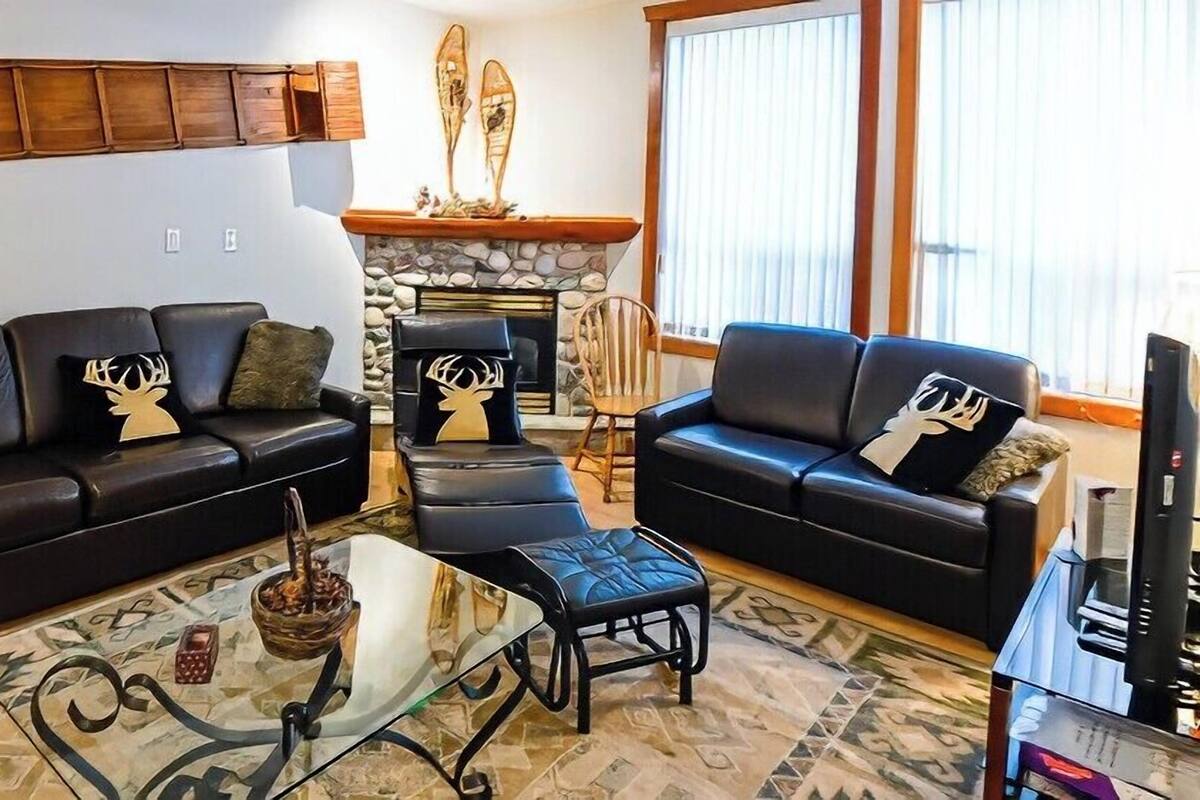A living room with two black leather sofas, a glass coffee table, and a stone fireplace.