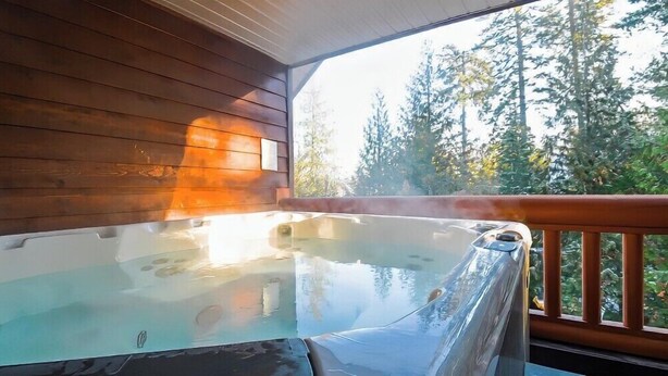 Een hottub op een houten terras met uitzicht op bomen.