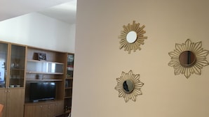Un salon avec un téléviseur, des meubles en bois et un canapé bleu. On y trouve trois miroirs fixés au mur, décorés de motifs en forme de soleil.