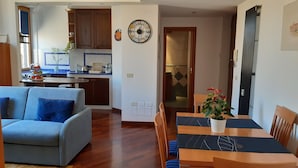 Un salon moderne avec un canapé, une table à manger et des chaises. On y trouve également un coin cuisine avec des placards et une horloge au mur.