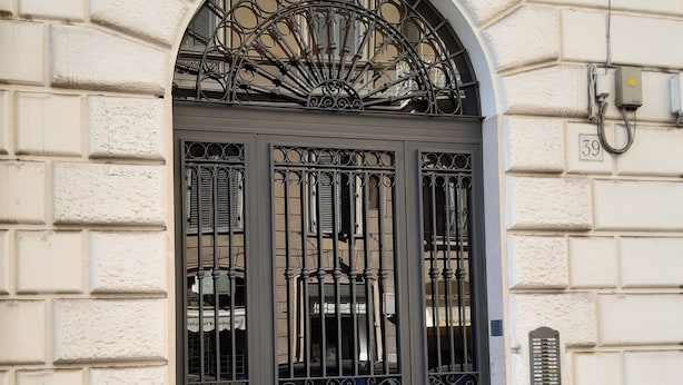 Une façade d’immeuble avec une grande entrée en arc de cercle, un portail en métal noir et une rue pavée.