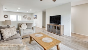A modern living room with a sofa, a wooden coffee table, a television on a cabinet, and a ceiling fan. - Spacious Oceanside Family Home w/ Fenced-In Yard (Oceanside)