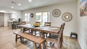 A spacious dining area with a wooden table and chairs, a small kitchen in the background, and decorative wall mirrors. - Spacious Oceanside Family Home w/ Fenced-In Yard (Oceanside)