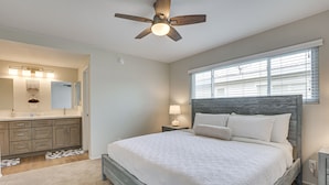 A bedroom with a bed, a ceiling fan, a nightstand, a lamp, and a window with blinds. - Spacious Oceanside Family Home w/ Fenced-In Yard (Oceanside)