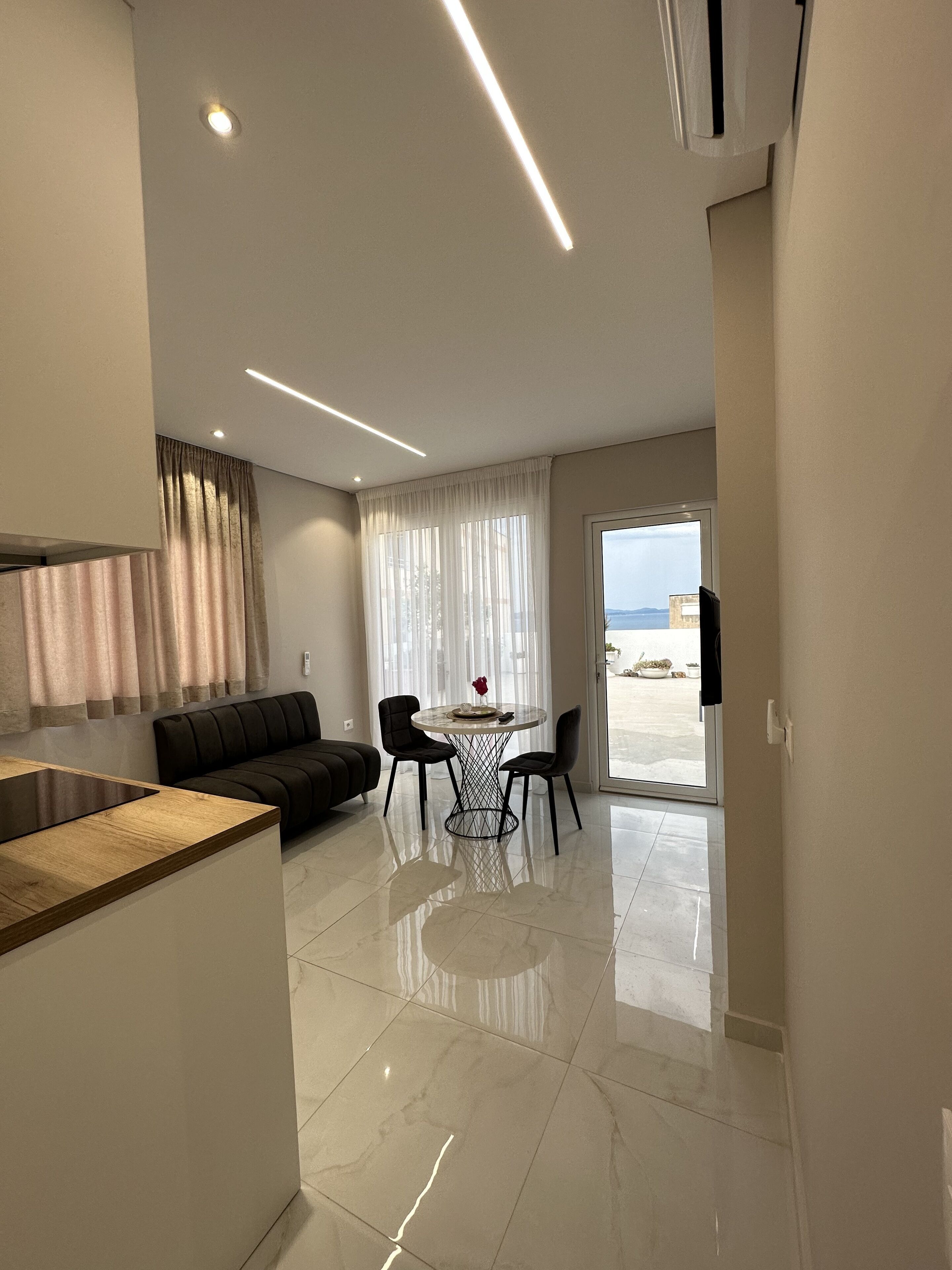 A modern kitchen with a built-in island, a dining area with a round table and chairs, and a view of the sea through large windows.