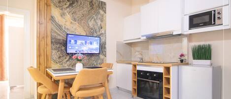 A modern kitchen with a built-in oven, microwave, and dishwasher. There is a dining area with a table and chairs, and a flat-screen TV mounted on the wall.