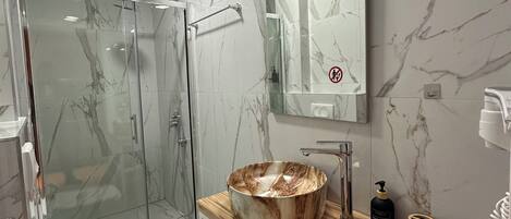Un baño moderno con cabina de ducha acristalada, suelo de mármol, tocador de madera con un lavabo grande y un inodoro.
