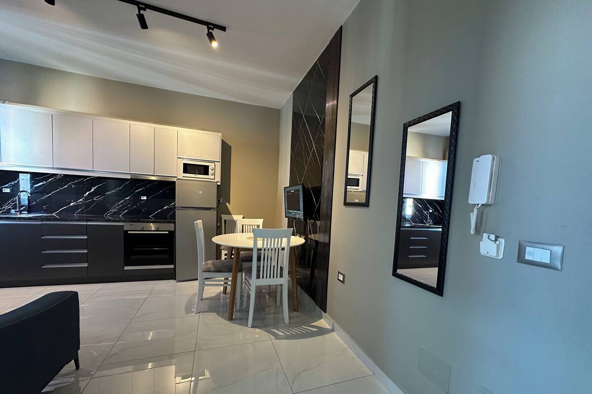 Une cuisine moderne avec des meubles blancs, un plan de travail en marbre noir et un coin repas comprenant une table et des chaises blanches.
