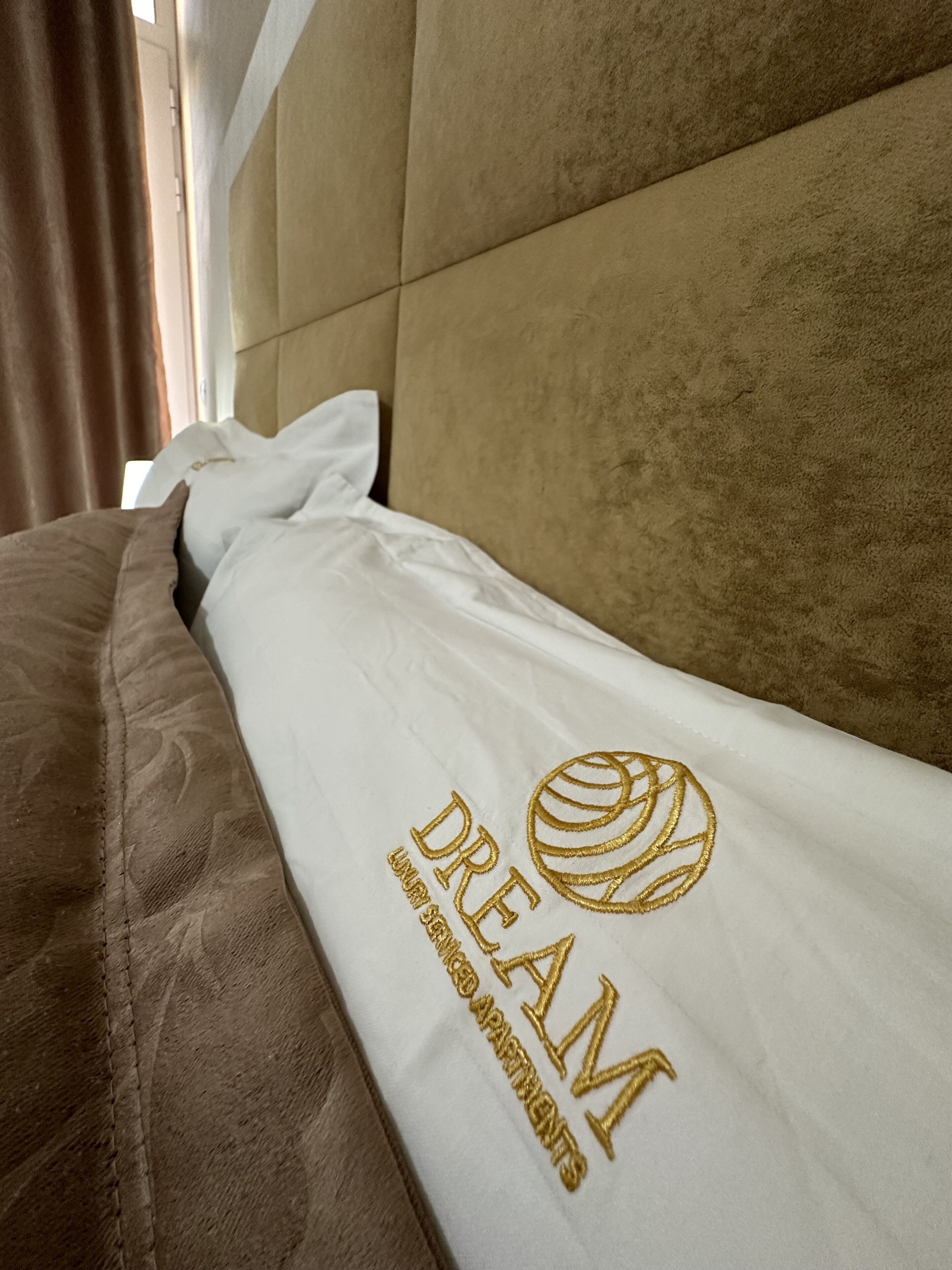 Una cama con un almohadón y una manta blancos, con texto bordado y un diseño de pelota de baloncesto.