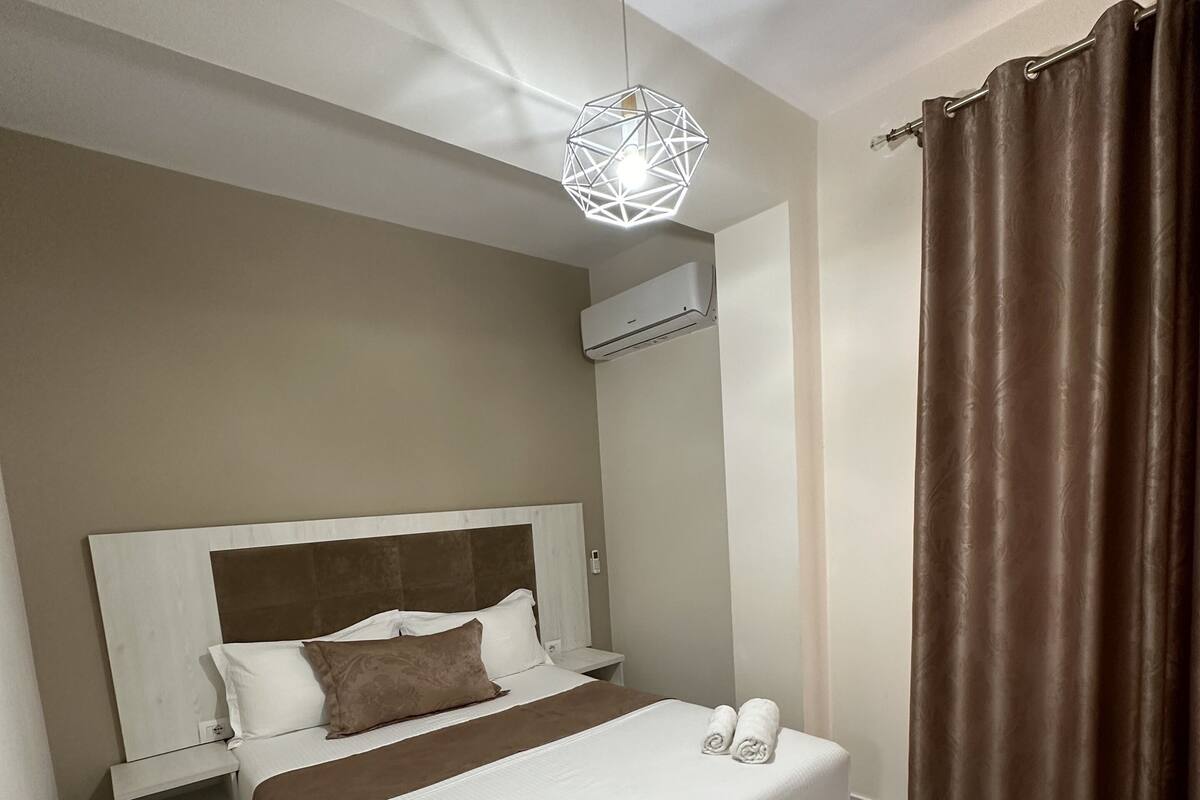 Une chambre moderne avec un grand lit, une table de chevet, un luminaire suspendu et un appareil de climatisation.