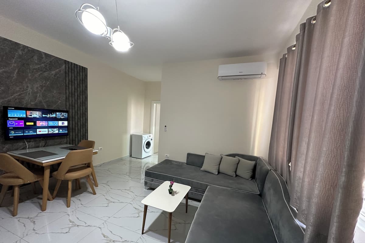 Un salon moderne avec un téléviseur à écran plat, un canapé, une table à manger avec des chaises et une petite table blanche.