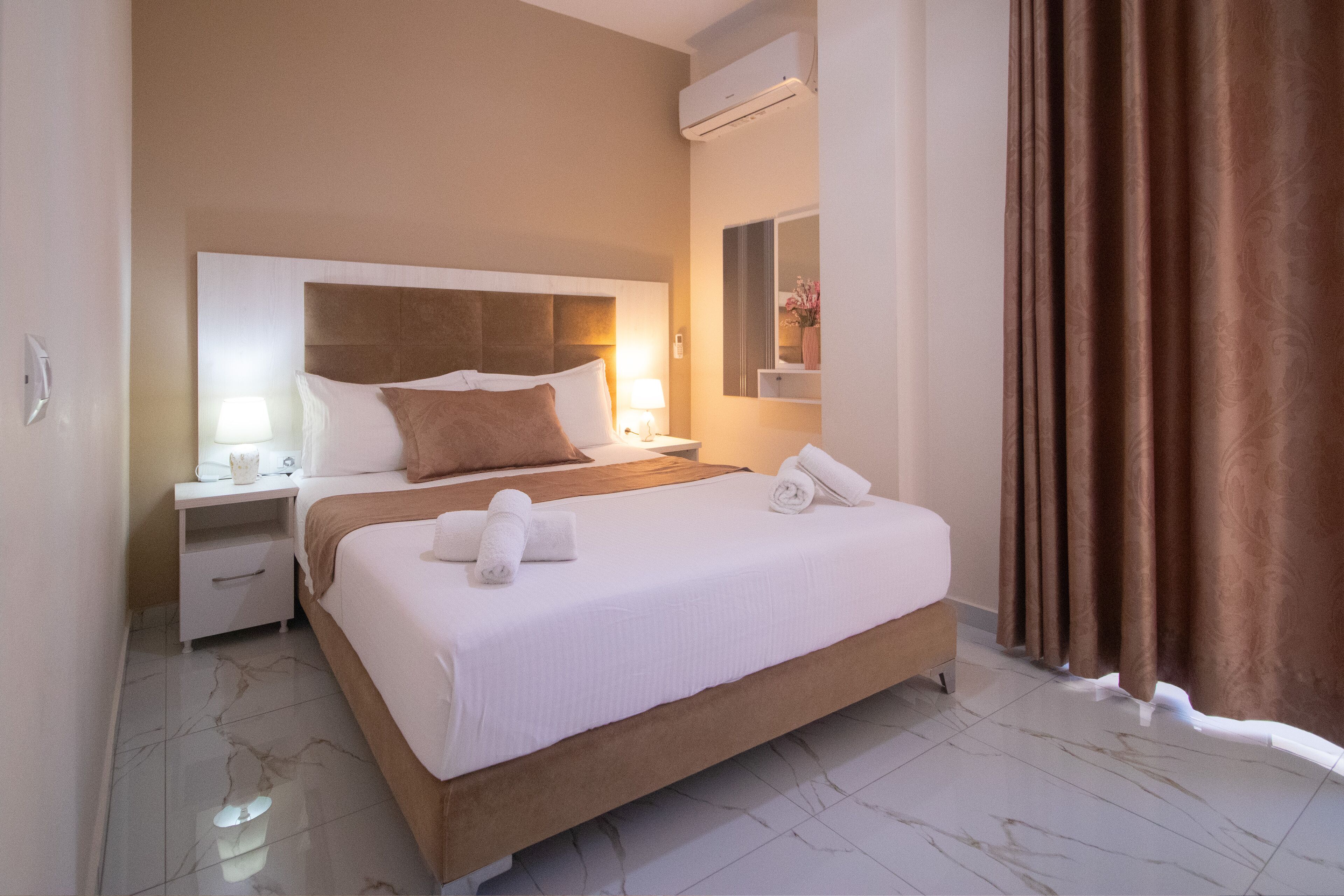 Ein Hotelzimmer mit einem großen Bett, zwei Nachttischen, einer Klimaanlage, einem Spiegel und einem Vorhang.
