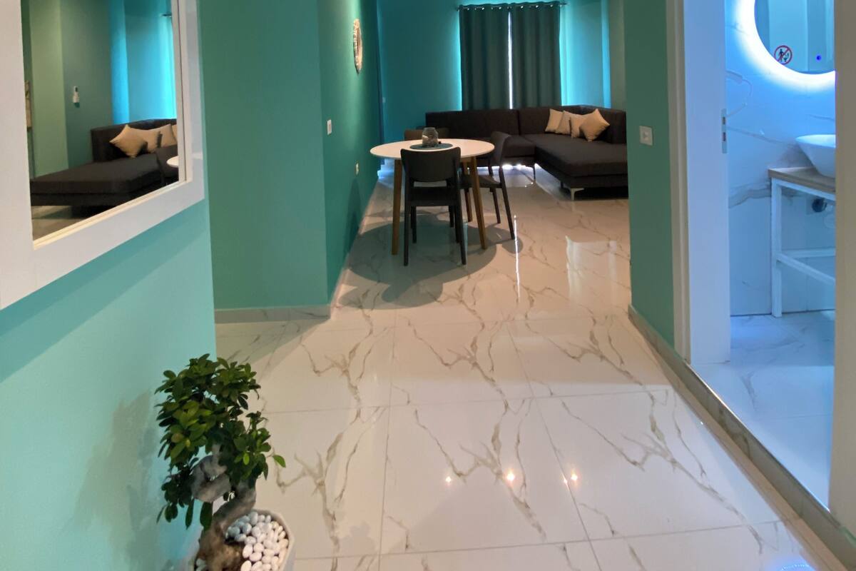 Un salon moderne avec des murs de couleur turquoise, un sol en marbre, un coin repas avec une table et des chaises, un canapé et une plante en pot.