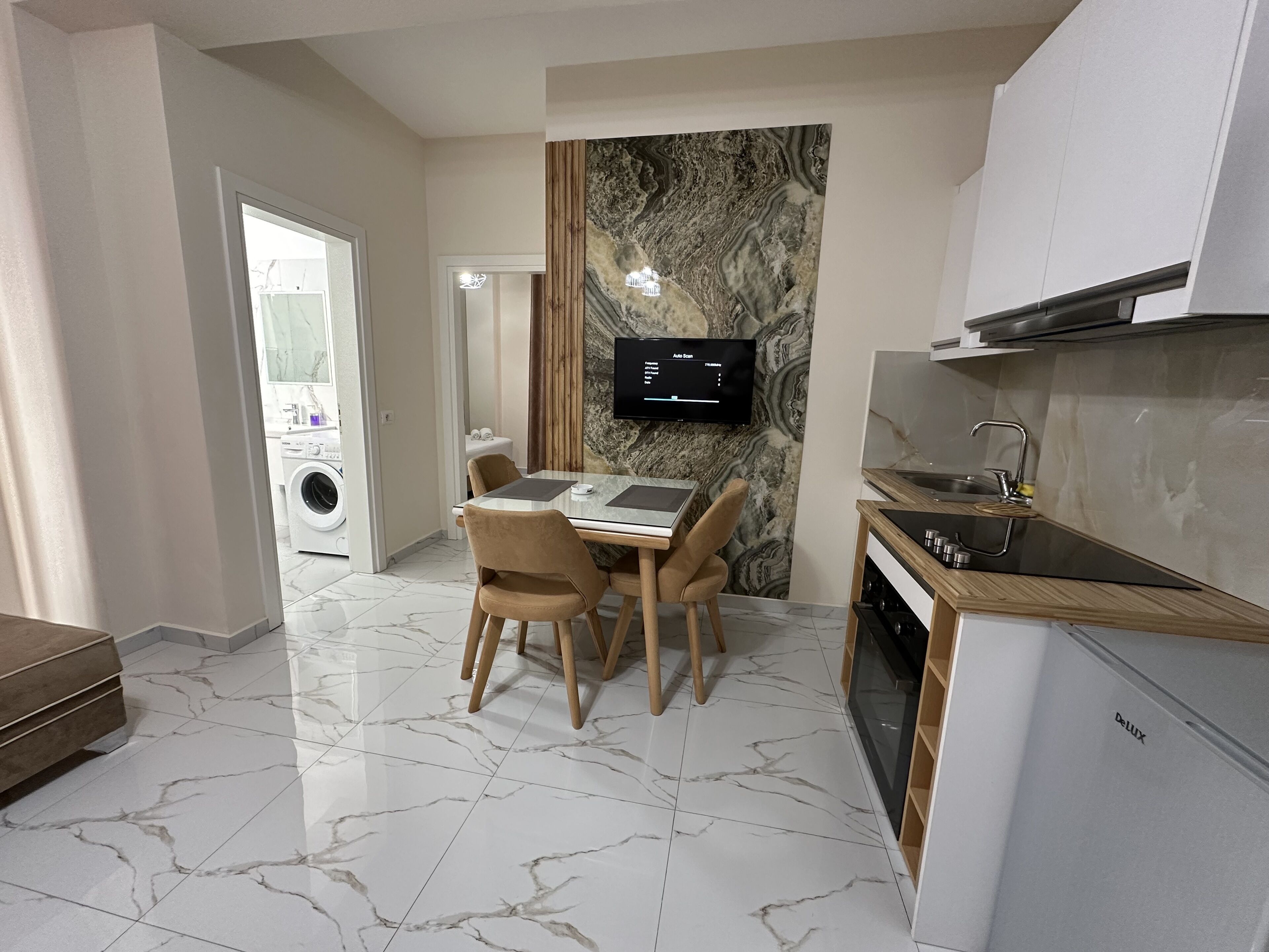 Una cocina moderna con horno integrado, un comedor con suelo de mármol y un televisor montado en la pared.