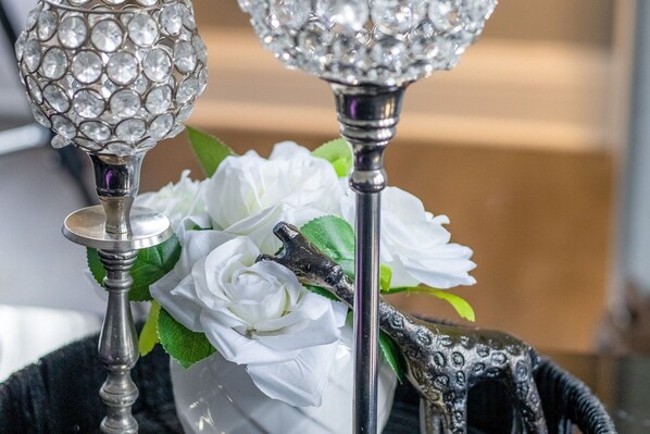 A decorative silver candle holder with a crystal top, a white flower arrangement, and a small animal figurine.