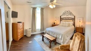 A bedroom with a bed, bedside tables, a wooden dresser, a ceiling fan, and a window with curtains. - Cozy Cottage (Pigeon Forge)