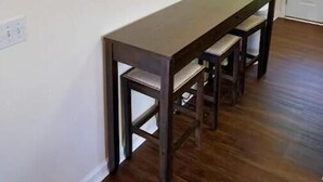 A dining area with a long wooden table and benches, two wall-mounted lights, and a white door in the background. - Cozy Cottage (Pigeon Forge)
