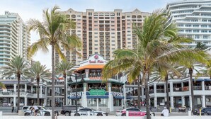 Un hotel frente a la playa con un bar y restaurante en la arena, palmeras y un coche patrulla estacionado al frente.