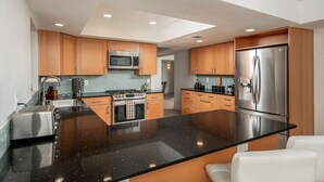 A modern kitchen with wooden cabinets, a stainless steel refrigerator, and a black granite countertop.