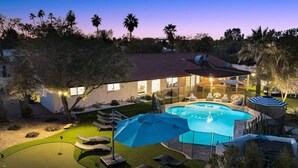 A backyard with a swimming pool, lounge chairs, and a small putting green.