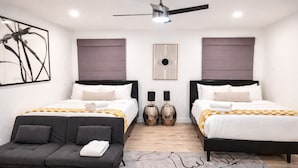 A modern hotel room with two beds, a sofa, and a ceiling fan.