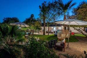 A well-lit outdoor area with umbrellas, a chess table, and a pool. - Lux Villa|Tennis+Pickleball+Golf+Basketball+4Suite (Scottsdale)