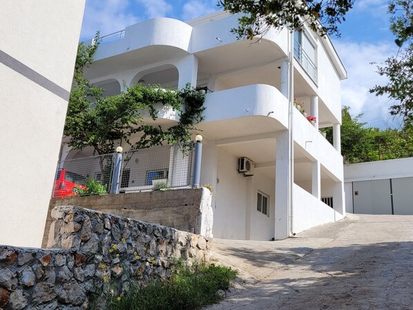 A modern multi-story building with balconies, a stone retaining wall, and a paved courtyard.