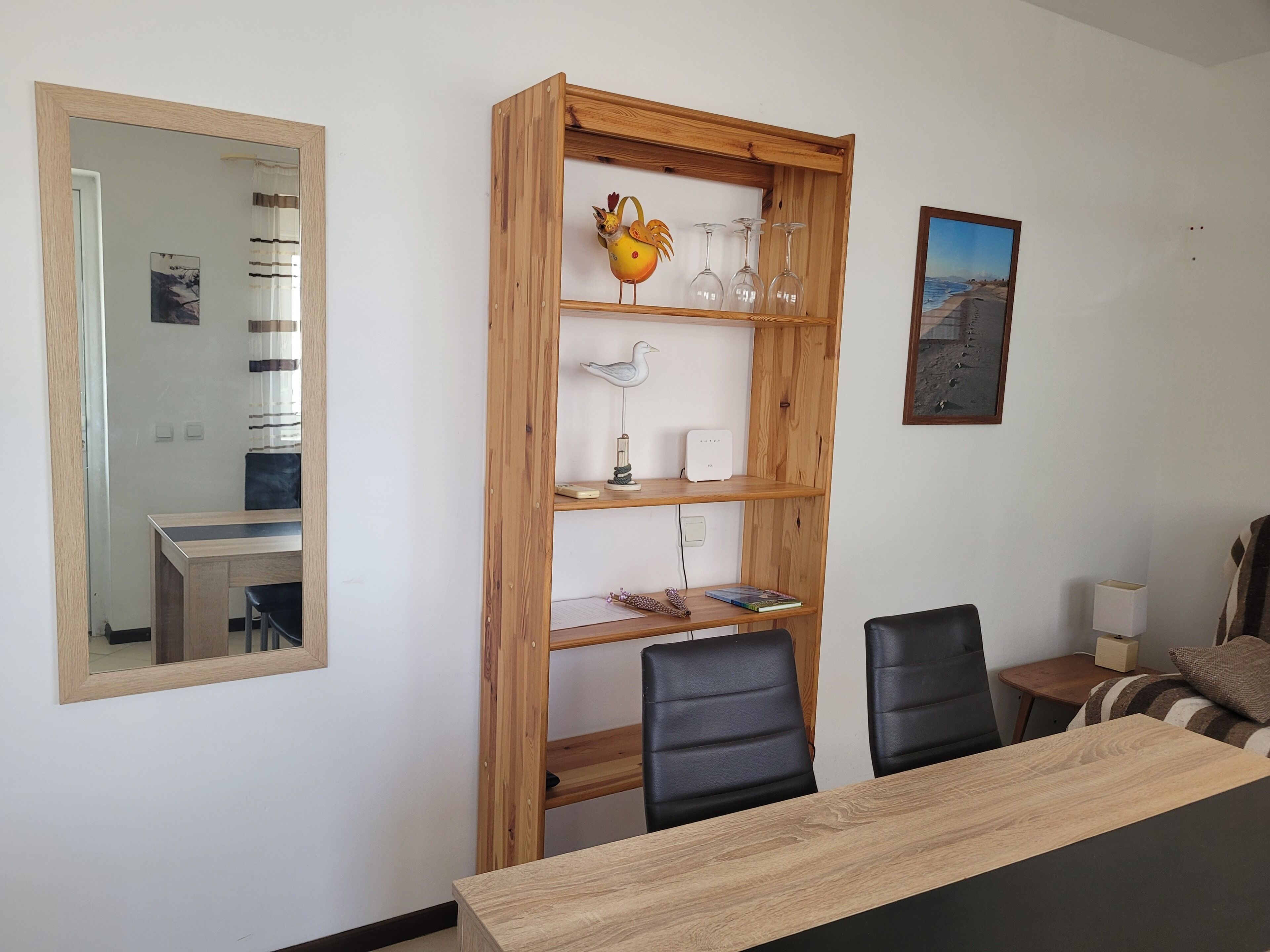 Un comedor con una mesa y sillas de madera, una estantería de madera con adornos, un espejo y un cuadro en la pared.