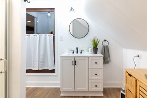 Een badkamer met een wit wastafelmeubel, een ronde spiegel, een plant in pot en een handdoek aan de muur.