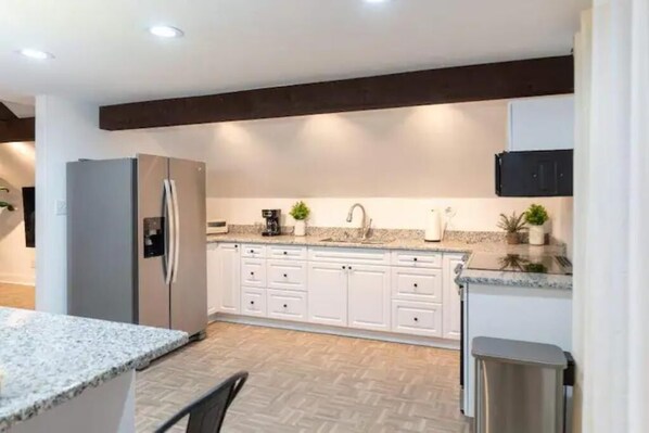 A modern kitchen with white cabinets, a granite countertop, and a stainless steel refrigerator.