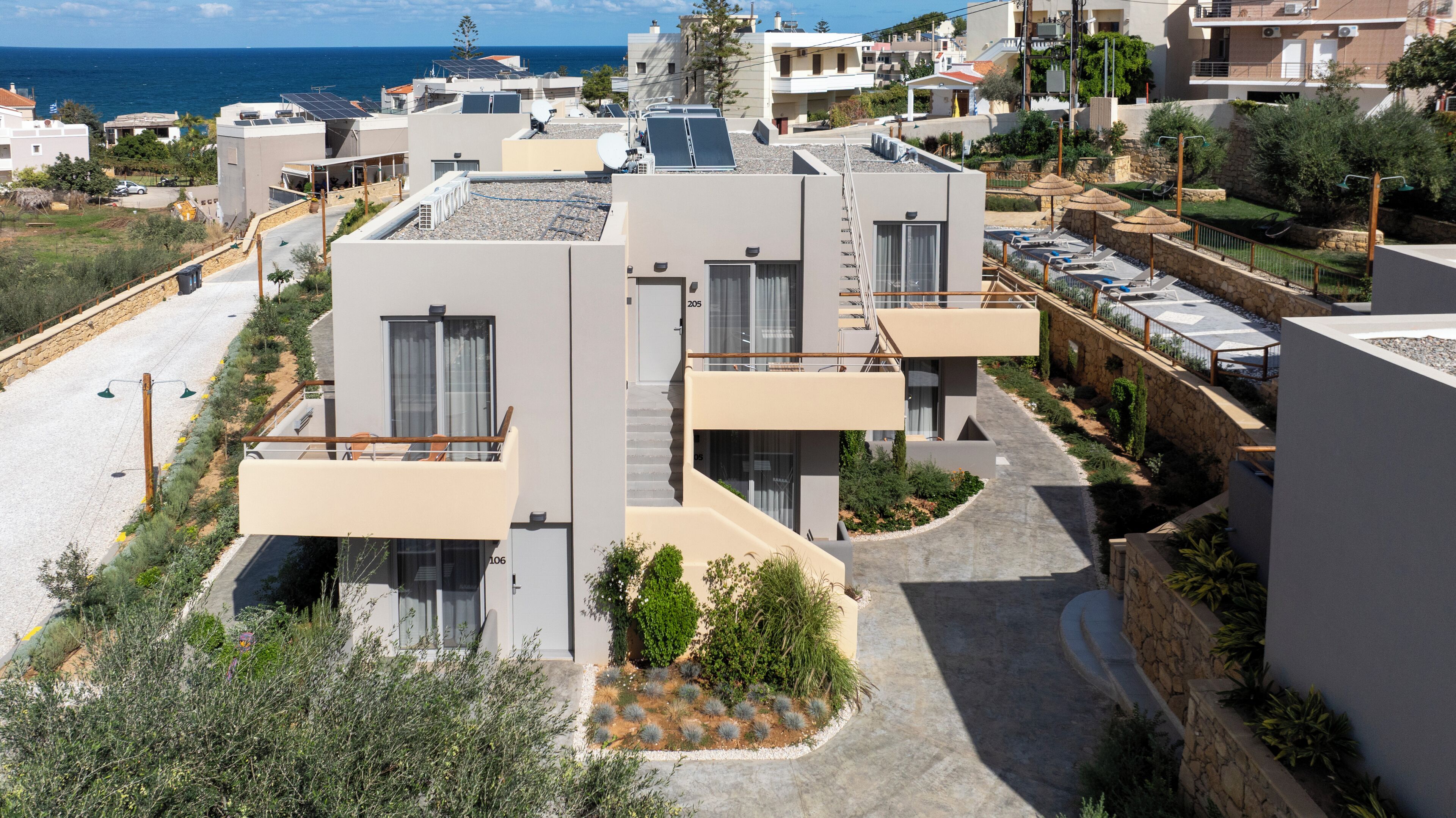 A modern residential building with multiple balconies, a paved driveway, and a view of the sea.