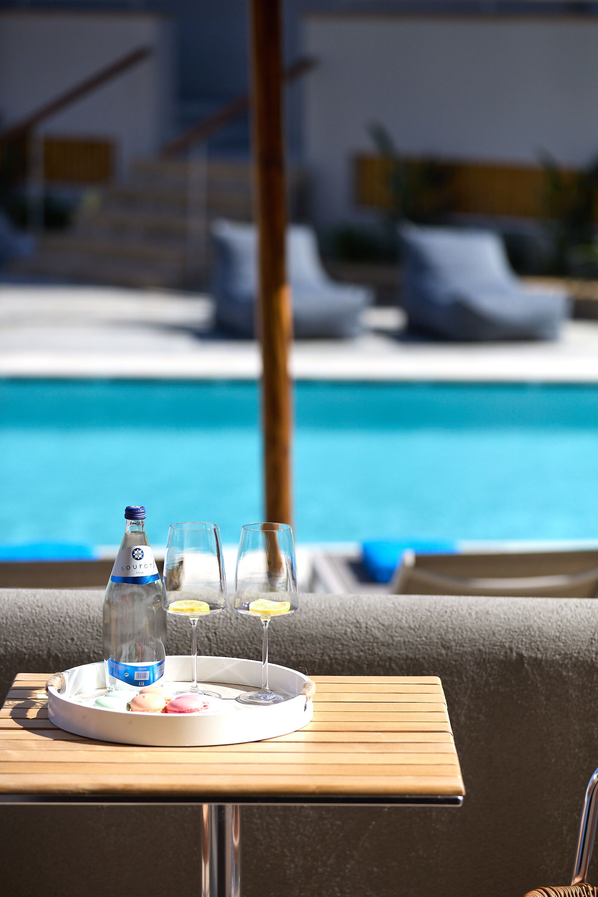Una mesa con una botella, vasos y una bandeja de comida junto a una piscina.
