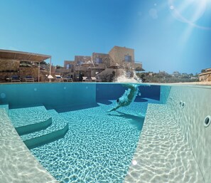 A clear pool with a diving board and lounge chairs, surrounded by buildings. - Villaggio Mare Suites (Chania)
