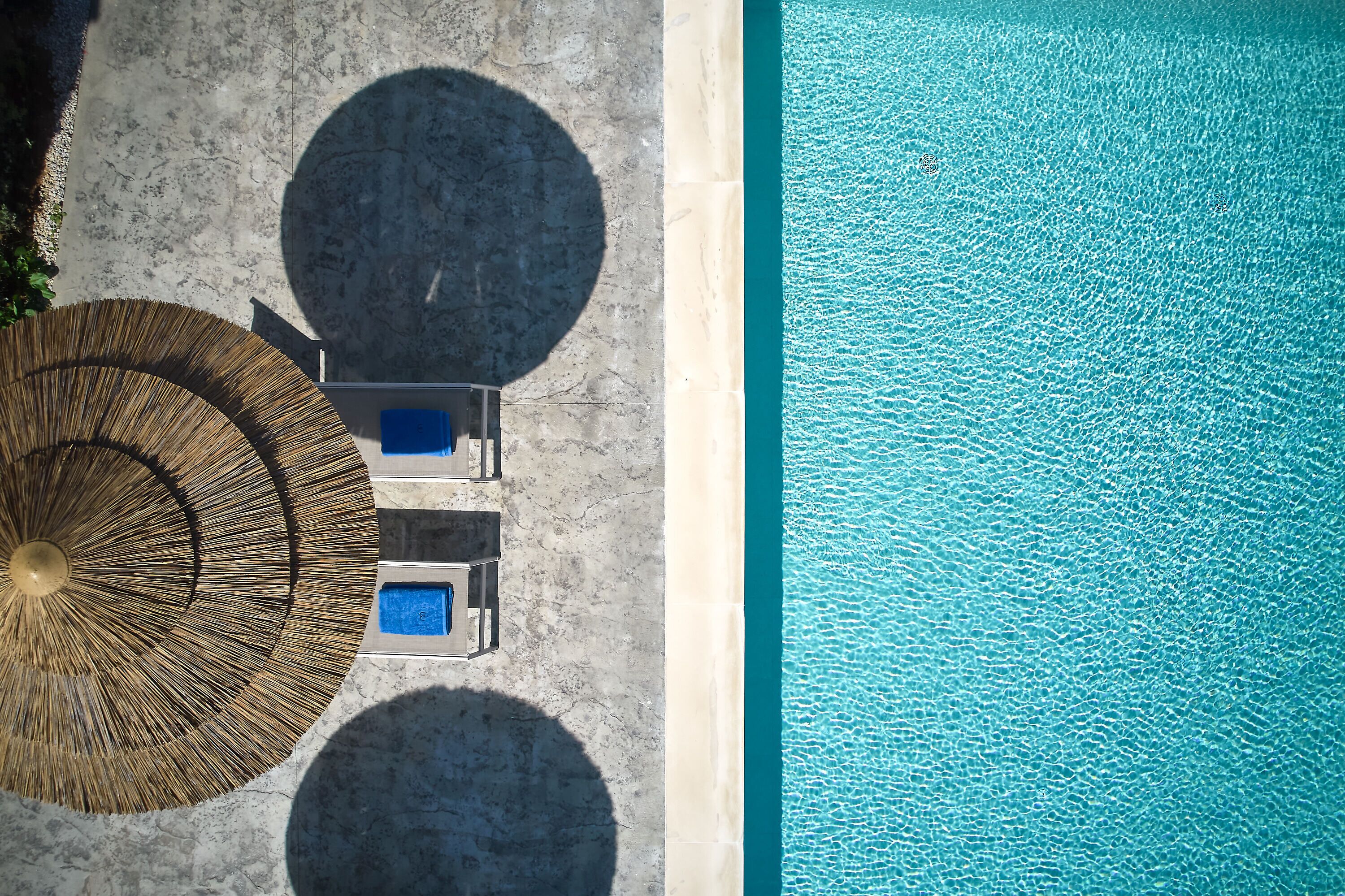 Vista aérea de un área junto a la piscina con una sombrilla circular, dos sillas de descanso y una piscina azul cristalina.