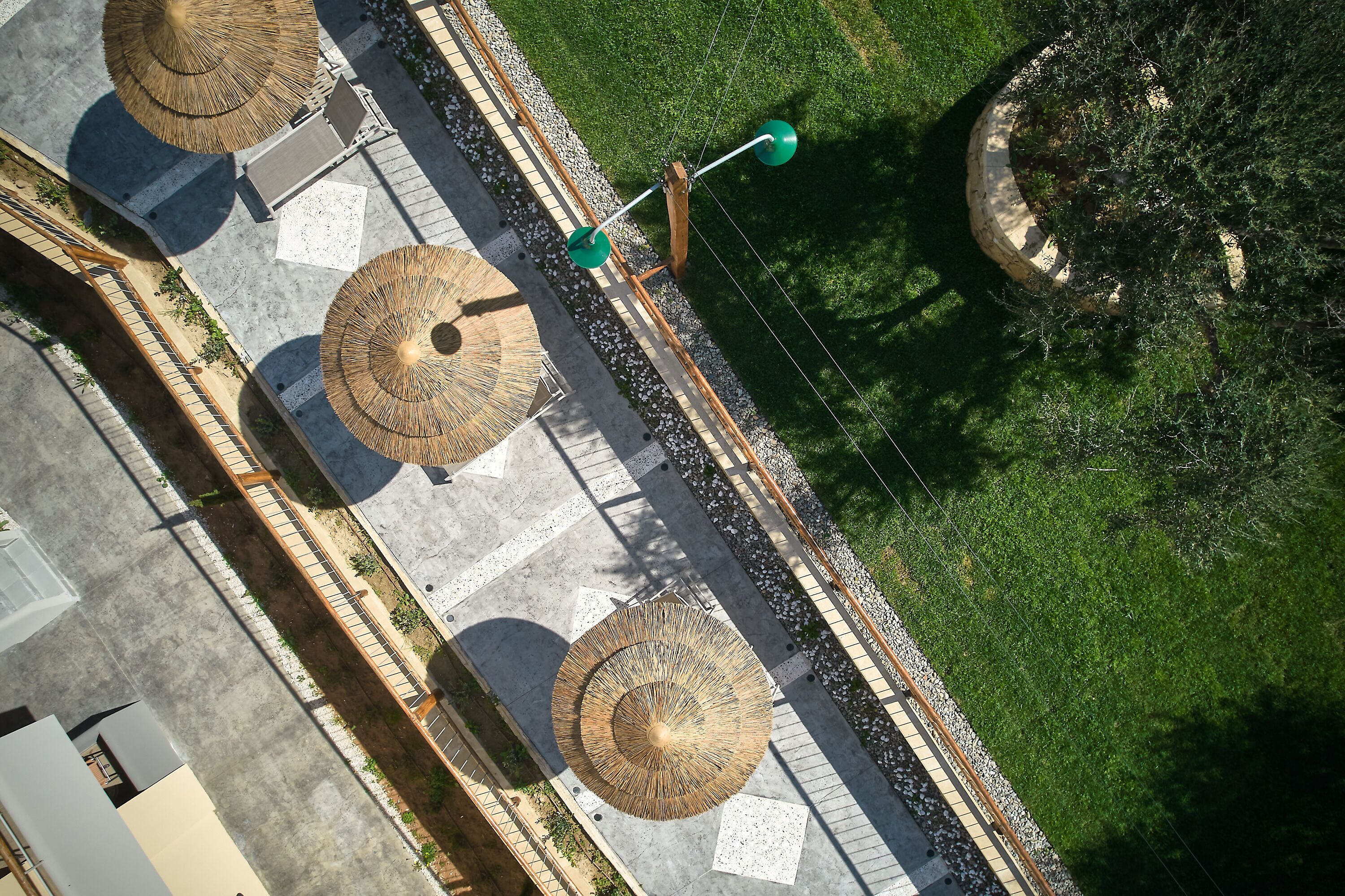 An aerial view of a pathway with thatched umbrellas, a concrete walkway, and a grassy area.