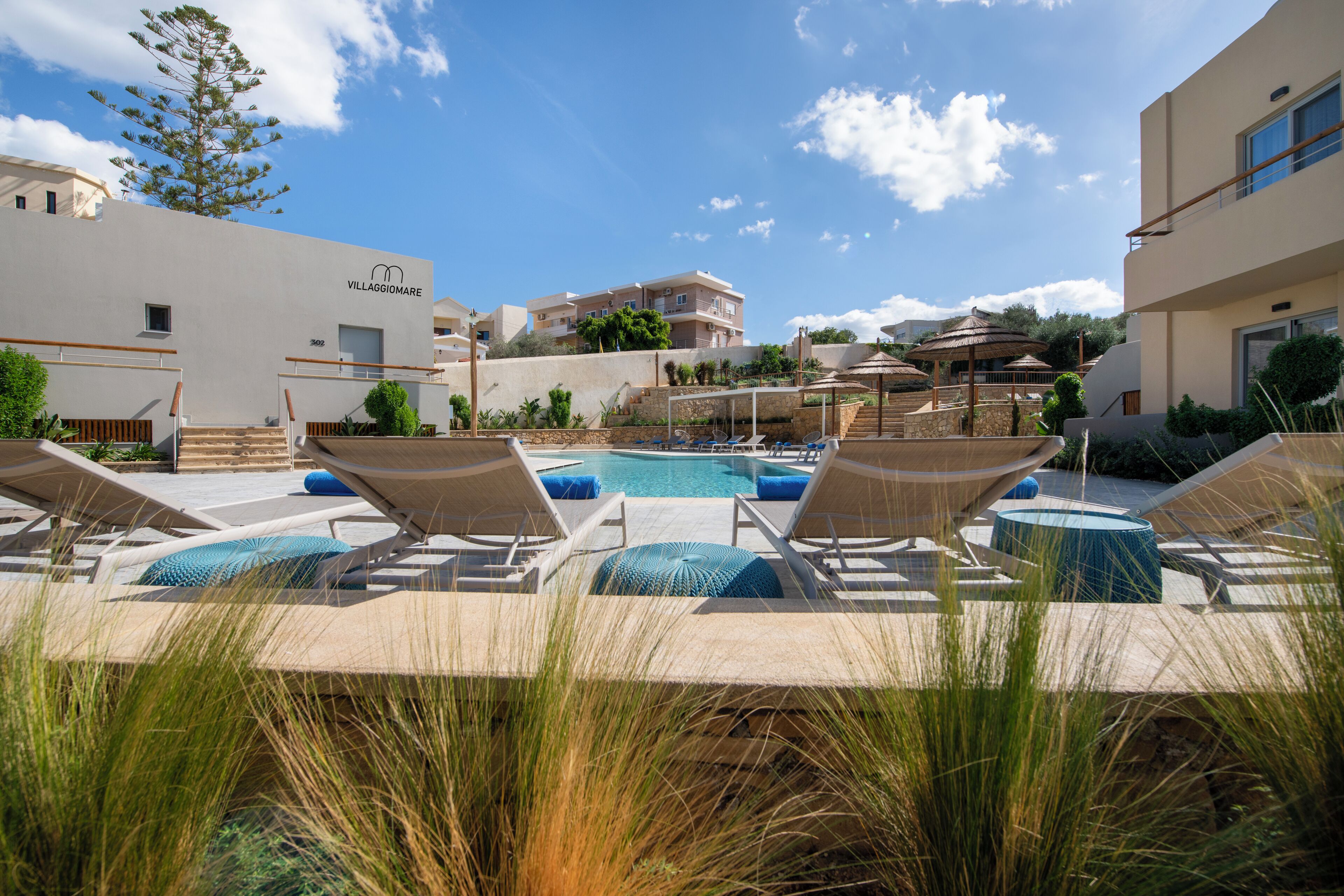 A pool area with lounge chairs and umbrellas, surrounded by buildings with a sign reading "VILLAGGIOMARE".