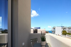 A balcony with a potted plant, a bench, and a view of buildings and the sea. - Villaggio Mare Suites (Chania)