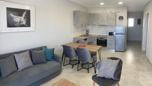 A modern living room with a grey sofa, a wooden coffee table, and a dining area with a wooden table and grey chairs. - Example Villa Southern Crete (Ierapetra)