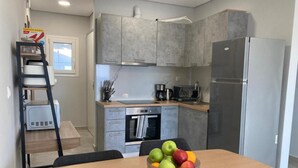 A modern kitchen with grey cabinets, a stainless steel refrigerator, and a wooden dining table with a bowl of fruit. - Example Villa Southern Crete (Ierapetra)