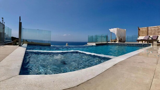 A rooftop infinity pool with clear blue water, a view of the ocean, and a glass-enclosed lounge area. - Example Villa Southern Crete (Ierapetra)