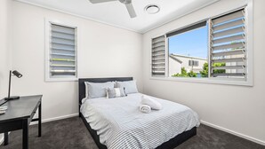 A bedroom with a bed, a desk, and two windows with shutters. - Villa Marguerite - walking distance to the beach (Coolum Beach)