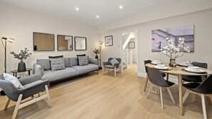 A modern living room with a grey sofa, a dining table with chairs, and a staircase leading to another level. - NEW LISTING!!! South Kensington Style newly refurbished apartment (London)